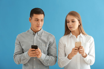 Young couple with mobile phones on color background