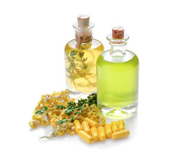 Bottles of essential oil with color capsules, flowers and thyme on white background