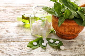 Mortar with fresh basil and pills in jar on wooden table