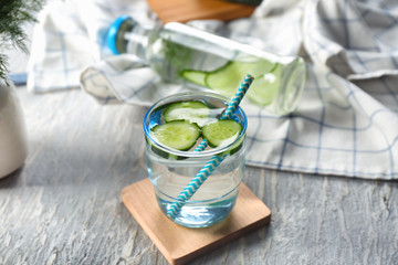 Glass of fresh cucumber water on light wooden table