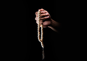 Male hands praying using prayer beads over dark backgroud