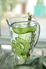 Jug of fresh cucumber water on table