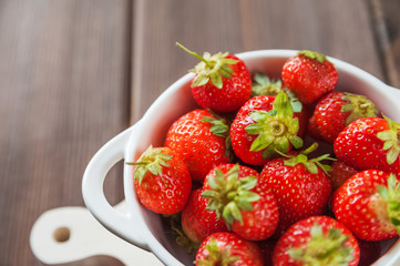 White plate with fresh ripe juicy strawberries on a wooden texture board