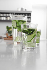 Glass of fresh cucumber water on white table in kitchen