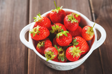 White plate with fresh ripe juicy strawberries on a wooden textural table close up