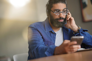 Hipster guy using smartphone and bluetooth headset