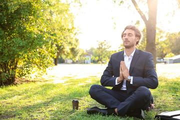 Handsome young businessman meditating in park