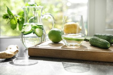 Glass and jug of fresh cucumber water with ingredients on grey table