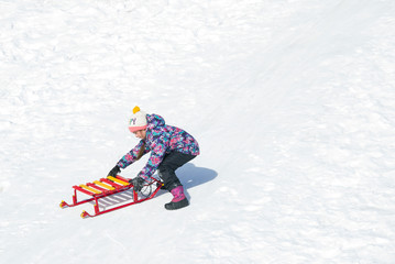 Cute little girl sliding on a sled on snowy hill. Active leisure outdoors in winter