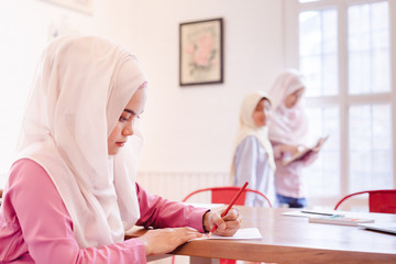 Beautiful young muslim teacher and cute asian muslim girls standing and reading a book in classroom.