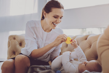 Immersed mother. Caring mother feeling immersed in playing with baby toys while taking care of her...