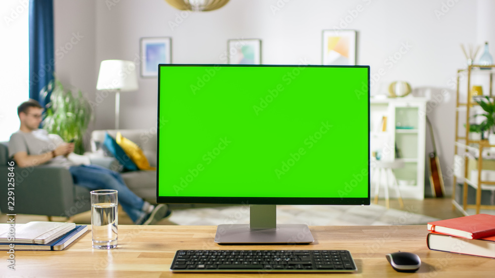 Poster modern personal computer with green mock-up screen display standing on the desk in the cozy living r