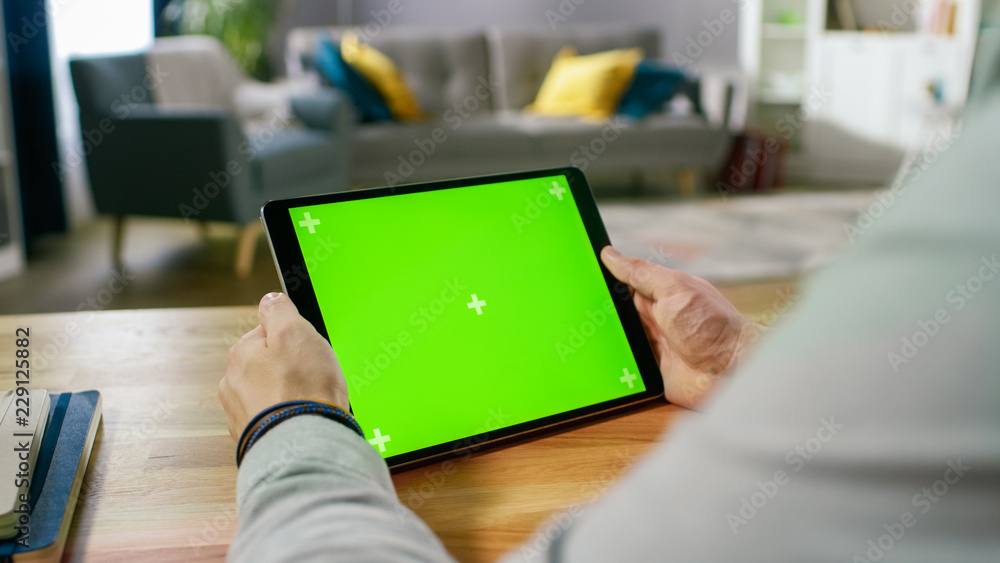 Poster man holding and watching green mock-up screen digital tablet computer while sitting at the desk. man