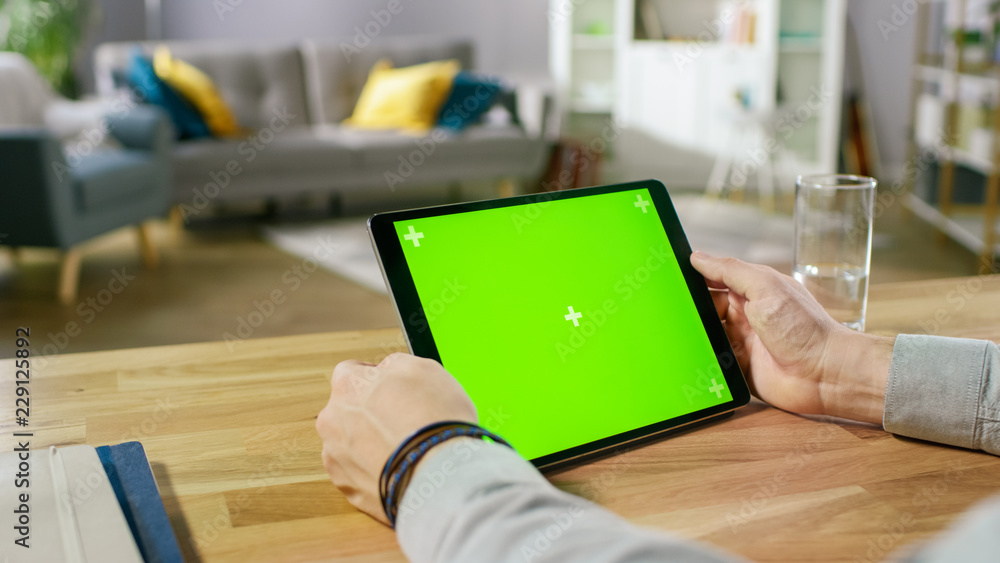 Poster man holding green mock-up screen digital tablet computer while sitting at the desk. man buying stuff