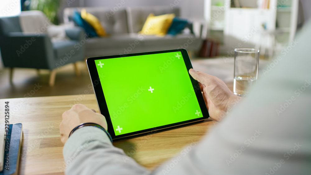 Poster man holding green mock-up screen digital tablet computer while sitting at the desk. man buying stuff