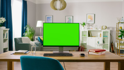 Modern Personal Computer with Mock-up Green Screen Display Standing on the Desk of the Cozy Home...