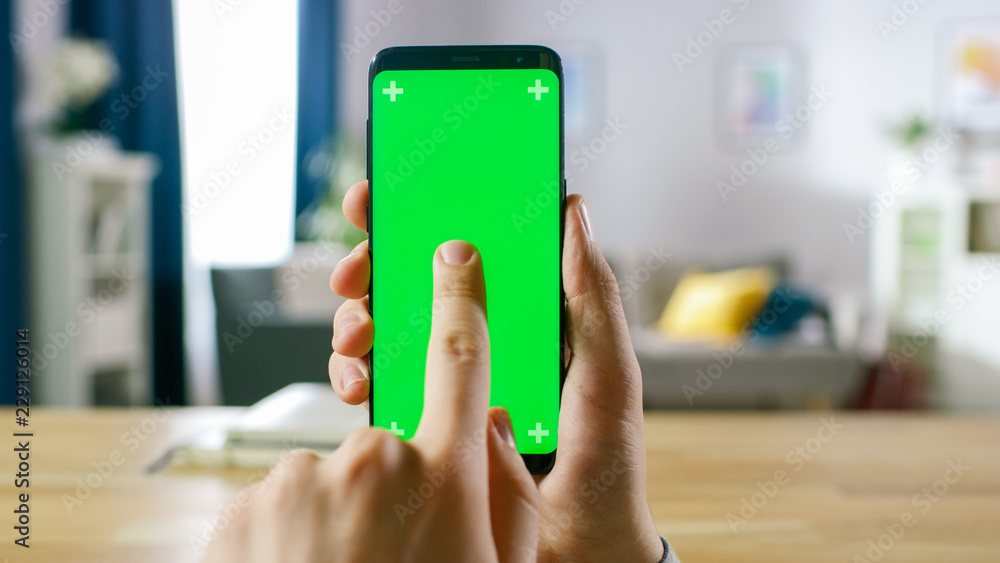 Poster close-up of a man holding green mock-up screen smartphone and using touchscreen gestures. touching m