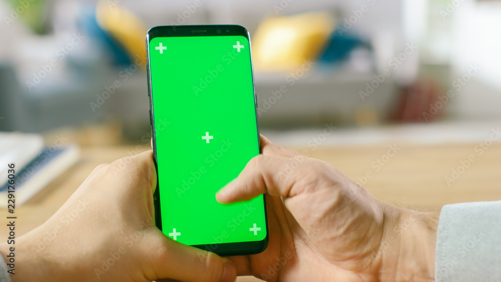 Poster close-up of a man uses green mock-up screen smartphone and does touchscreen gestures. touching mobil