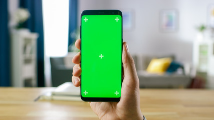 Close-up of a Man Holding Green Mock-up Screen Smartphone. Mobile Phone has Chroma Key Screen. In the Background Cozy Homely Atmosphere.