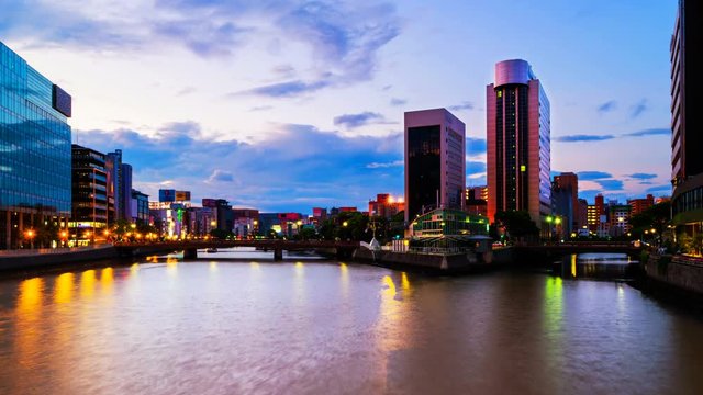 Fukuoka, Japan. A timelapse video of a sunrise in central Fukuoka, Japan, with a view of the Naka river, illuminated prominent skyscrapers and a clody colorful sky. Zoom in