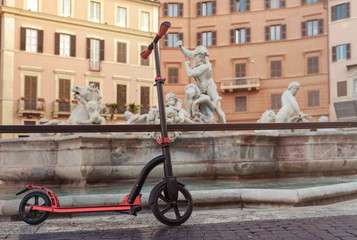 Red push scooters against the backdrop of the Fountain de Neptune on Piazza Navona in the Roma,...