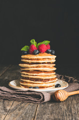 Pancakes with berry fruits, honey and mint leaf on rustic wooden table. Vertical, copy space for text © Vladislav Noseek