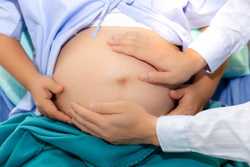 Handsome doctor is checking fetal position by touching pregnant woman belly at hospital. Beautiful mother or pregnant woman is pregnant nine month and nearly give birth. She stay at hospital room