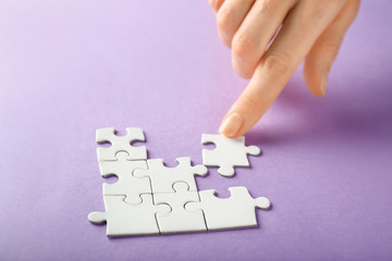 Hand of woman doing puzzle on color background, closeup