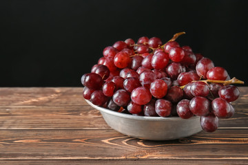Bowl with juicy sweet grapes on wooden table