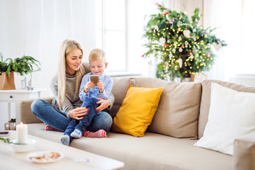 A mother and small boy with smartphone sitting on a sofa at home at Christmas time.