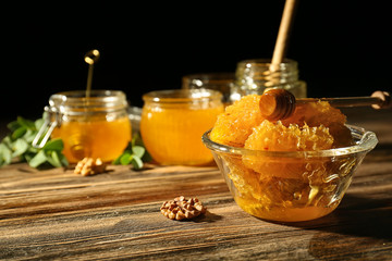 Bowl with sweet honeycomb and dipper on wooden table against dark background