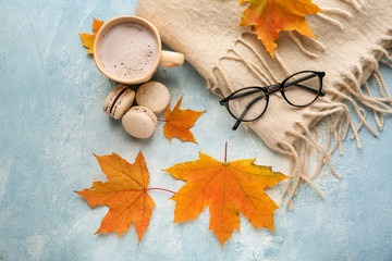 Composition with cup of aromatic coffee, warm plaid and autumn leaves on color background