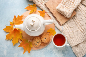 Composition with cup of aromatic tea, warm sweater and autumn leaves on color background