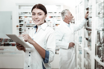 Female pharmacist. Beaming blue-eyed appealing dark-haired female pharmacist wearing white coat...