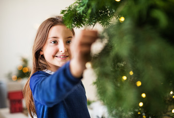 Small girl standing by a Christmas tree at home. Copy space.