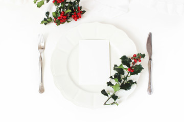 Traditional Christmas table place setting. Silver cutlery, holly berry branches, porcelain plate...