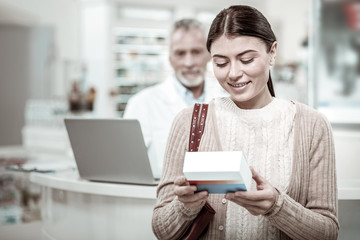 Good vitamins. Beaming dark-haired woman feeling pleased after buying good vitamins while leaving drugstore