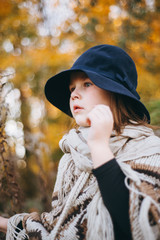 Outdoor portrait of a cute little girl in an autumn forest, wearing knitted poncho and hat. Autumn mood in the forest. Atmospheric walk through the forest of a beautiful girl