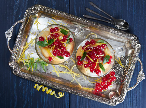Two glass cups of limoncello (or limoncino) tiramisu topped with redcurrants and mint leaves, on a silver tray set on a dark background