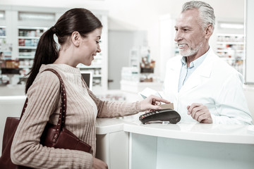 Obraz premium Paying by card. Dark-haired beautiful stylish client of drugstore paying for her order by card after buying favorite vitamins