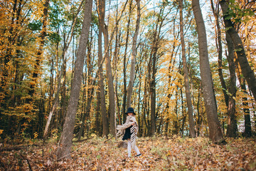 Fototapeta premium Outdoor portrait of a cute little girl in an autumn forest, wearing knitted poncho and hat. Autumn mood in the forest. Atmospheric walk through the forest of a beautiful girl