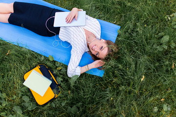 Girl resting in the park lying on the grass with a laptop and listening to music. Top wiew