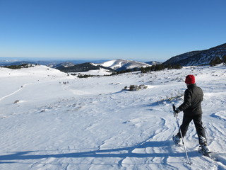 Fototapeta na wymiar Jeunes garçon en raquette en hiver en montagne dans la neige avec un bonnet rouge