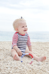 Adorable cheerful baby in striped bodysuit playing on the pebble beach