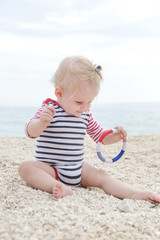 Adorable cheerful baby in striped bodysuit playing on the pebble beach
