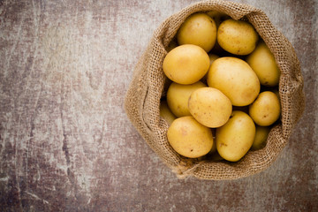 Sack of fresh raw potatoes on wooden background, top view.