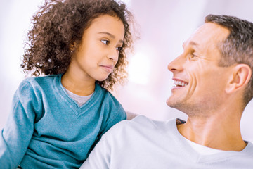 Fototapeta premium Lets joke. Emotional child looking at her dad while being at home together