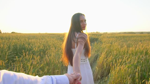 Follow me. Happy couple holding hands, running on golden wheat field and having fun outdoors. Couple walking on meadow. Young Man and beautiful woman, happy family in love. Sun flare. Slow motion