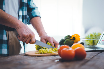 Food preparation. Close up of a nice handsome man using a knife while cutting lettuce