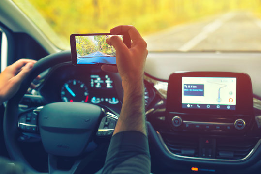 Male driver using smartphone to capture pictures of road, while driving